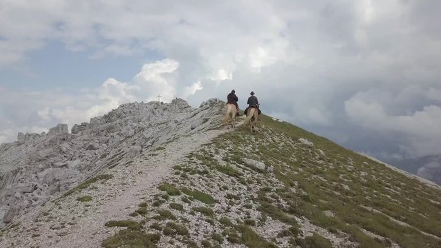 Two friends riding together over a ridge towards the summit of a mountain in the Dolomites.