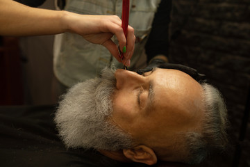 Shaving process of beards in Barbershop. Master makes a haircut beard client with vintage straight razor.