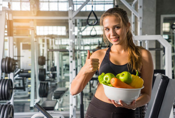 Fototapeta premium White women, beautiful women wearing sports, carrying vegetable plates, having green apples, carols and lifting their thumbs in the gym. Fitness and healthy lifestyle concept.
