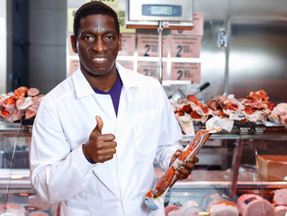 Successful butcher shop owner giving thumbs up, satisfied with quality of meat products