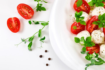 Caprese salad with ripe red cherry tomatoes, mozzarella cheese balls, young basil leaves, spices with sprouts of pea on a white background. Top view.