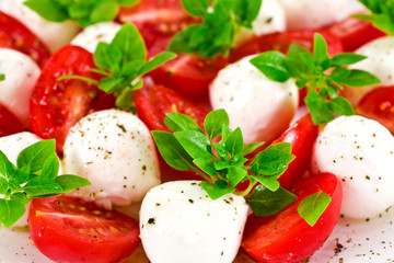 Caprese salad background. Ripe red cherry tomatoes, white mozzarella cheese balls with young basil green leaves and spices.
