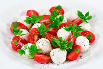 Caprese salad. Ripe red cherry tomatoes, mozzarella cheese balls with young basil leaves and spices.