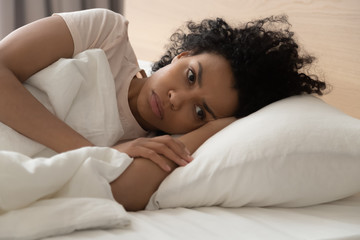 Unhappy African American woman suffering from insomnia, lying in bed