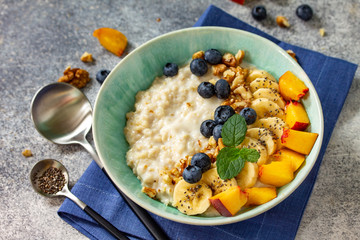 Healthy food for Breakfast, vegetarian and diet food concept. Oatmeal porridge with chia, banana, blueberry, fruits and nuts on a stone countertop.