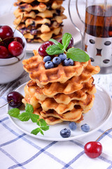 Stack of waffles topped with fresh bilberries, cherries and mint on the white wooden table