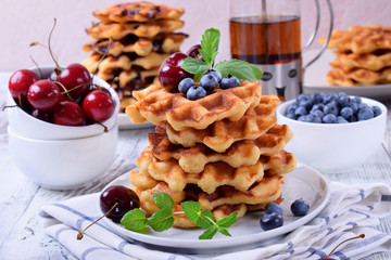 Stack of waffles topped with fresh bilberries, cherries and mint on the white wooden table
