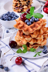 Stack of waffles topped with fresh bilberries, cherries and mint on the white wooden table