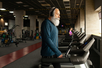 Fototapeta na wymiar Bearded Senior Man On Running Machine In Gym. Treadmill. 
