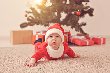 Obraz na płótnie Canvas Cute baby girl wearing santa claus suit crawling on floor over Christmas tree. Holiday season.