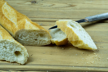 Freshly baked traditional french bread on a wooden table next to a kitchen knife. Sliced french baguette.