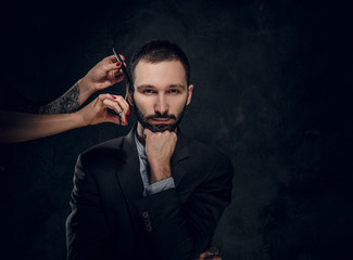 Successful confident male in classic suit is visiting a barbershop for beard trimming.