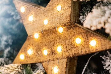 Decorative wooden star with lamps hanging on pine branches with festive background