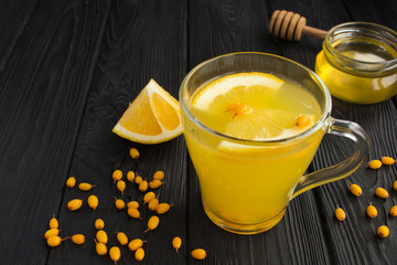 Sea buckthorn drink in the glass cup and honey on the black wooden background. Healthy medical drink.