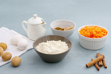Ingredients for baking carrot cake. Flour, grated carrots, eggs, milk, walnuts, spices are located on the kitchen table in gray. Carrot cake day