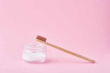 Wooden bamboo toothbrush and baking soda powder in glass jar on a pink background.  Teeth health...