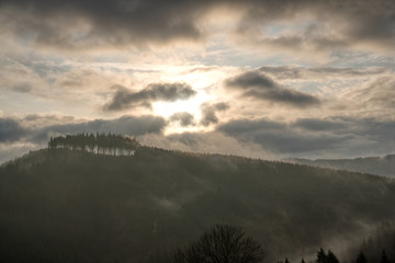 sun shining through the clouds in the mountains with fog on the hill