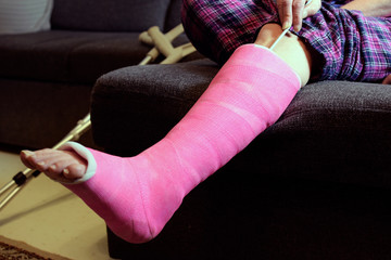 Foot itching under plaster cast. Woman scratching pink orthopedic cast with knitting needle. Space...