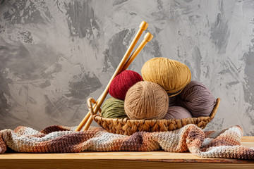 Skeins of yarn for knitting from natural wool in a wicker basket. Wooden surface or table. Background - concrete wall. Wooden knitting needles.