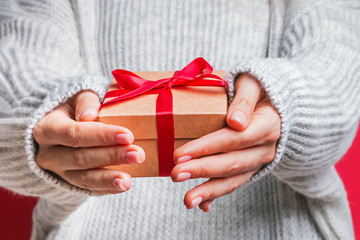 Female hands holding gift box with red ribbon close-up.