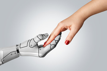 Robotic cyborg hand holding female human hand on gray background. People and artificial intelligence technology concept.