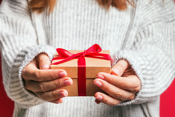 Woman wearing cozy winter sweater holding a giftbox with red bow close-up.