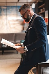 Fototapeta premium Stylish businessman standing near table in the office and reading documents