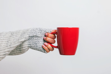 Woman's hand in cozy sweater holding a red coffee mug.