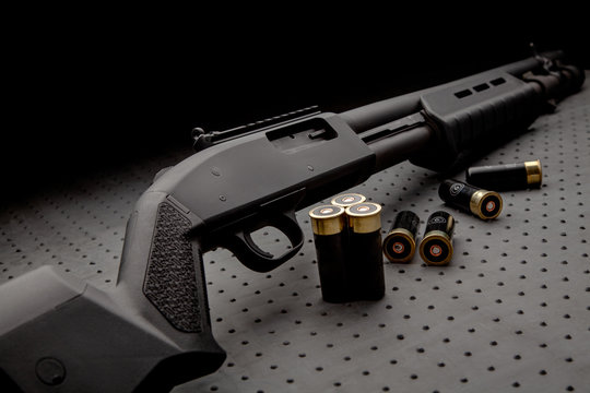 Modern black shotgun and ammo for him on a dark background.