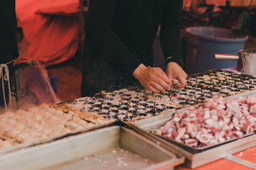 A man in long black sleeve shirt cooking Japanese Takoyaki. ( Ball-shaped Japanese snack )