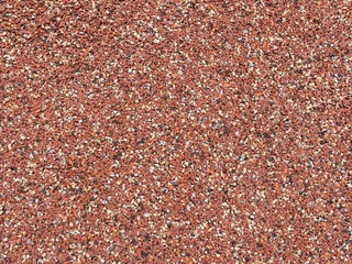 Photo background with rubber surface coating on an outdoor sportsground floor, with small particles in red, white, black, yellow color. Rubber safety surfacing texture.