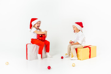 Two funny little kids in Santa hat sitting on gift boxes. Isolated on white background. Christmas and new year concept.