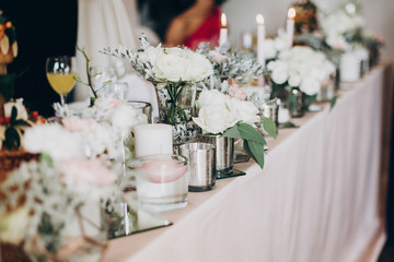 Candle, White  flowers in modern glass vase on pink centerpiece. Stylish luxury decor on wedding table.Luxury catering and adorning. Holiday feast