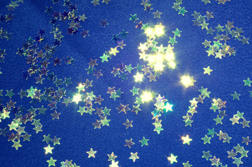 Sparkling stars on a blue fabric. Shiny fake stars (Christmas confetti).