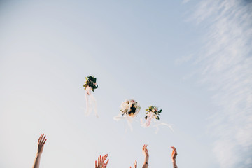 Bride and bridesmaids throwing wedding bouquets up in the sky in evening soft light. Stylish...