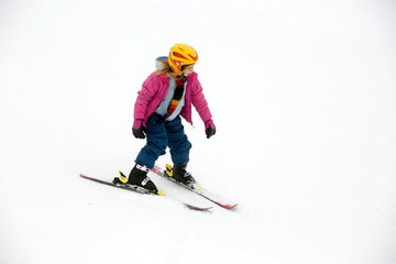 Fototapeta na wymiar Young active girl skies downhill without sticks in yellow helmet and pink coat. Cut out, separated by snow and fogy weater.