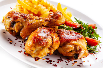Roast chicken drumsticks with french fries and vegetables on white background