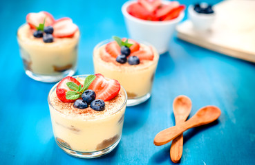 homemade, exquisite dessert tiramisu in glasses decorated with strawberry, blueberry, mint on blue wooden table