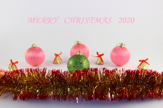 Merry Christmas 2020 pink text with pink and green festive balls, yellow bells and yellow red tinsel