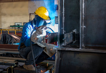 The welder is welding a column steel structure work with process Flux Cored Arc Welding(FCAW) and dressed properly with personal protective equipment(PPE) for safety, at industrial factory.