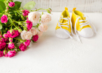 Children's yellow shoes, stands on a white table with roses. closeup. the concept of children's clothing. Greeting children form with yellow booties
