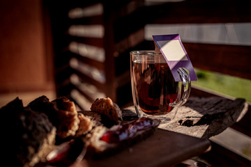 Glass of black tea in double bottom glass under the shade under sun light, winter hot drink with glass kettle of strong tea on wooden table and tea cloth, copy space