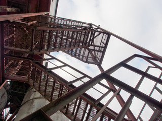 Technopathy, fragments of plant design and buildings. Metal staircases and columns of reinforced concrete products factory on the background of gray, cloudy sky.