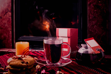 Hot tea or coffee in a red mug, ginger cookies on vintage wood table. Fireplace as background. Christmas or winter warming drink. Layout with free text space.