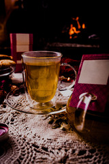 Hot tea or coffee in a red mug, ginger cookies on vintage wood table. Fireplace as background. Christmas or winter warming drink. Layout with free text space.