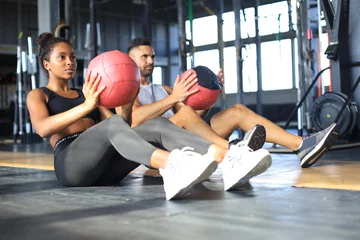 Rolgordijnen Beautiful young sports couple is working out with medicine ball in gym. © ty