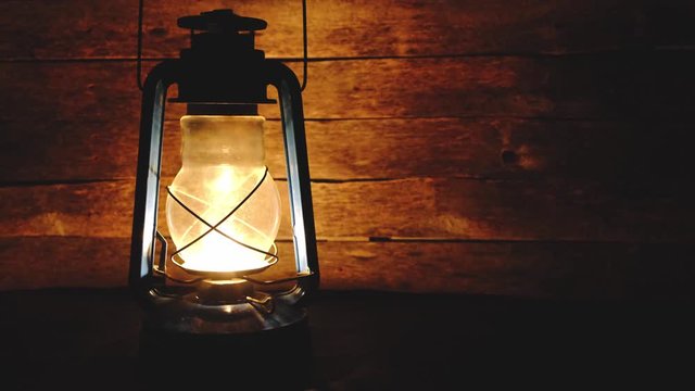 Kerosene lamp burns in the dark, sways in the draft and illuminates a wooden background of boards.