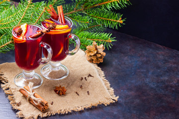 Red mulled wine and fir branches on burlap. Mulled wine with oranges, honey, cinnamon and cloves on a dark background. Hot wine with honey and spices