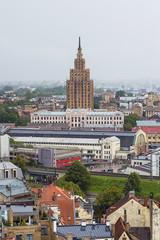 Obraz premium Aerial view of Latvian Academy of Sciences, Riga Central Market, Bus station and Riga Old Town from Saint Peter church on foggy and rainy day, Riga, Latvia. Stalin-era skyscraper. Soft focus