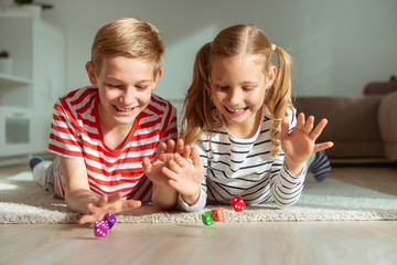 Portrait of two cheerful children laying on the floor and playing with colorful dices
